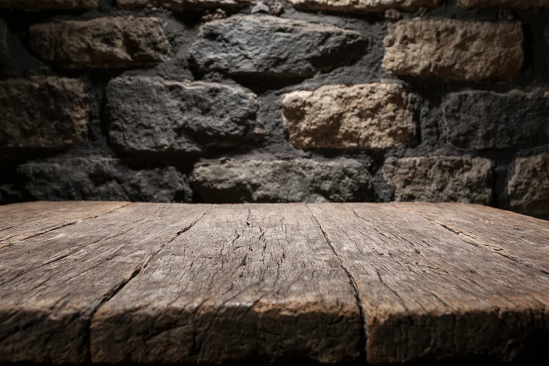 Weathered wooden table surface in front of dark stone wall with copyspace