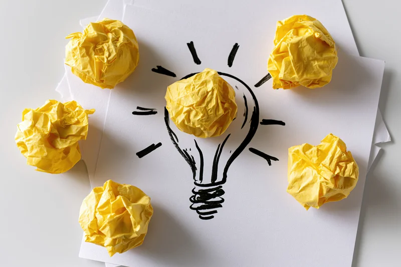 Crumpled yellow paper balls arranged around a hand-drawn lightbulb on white paper