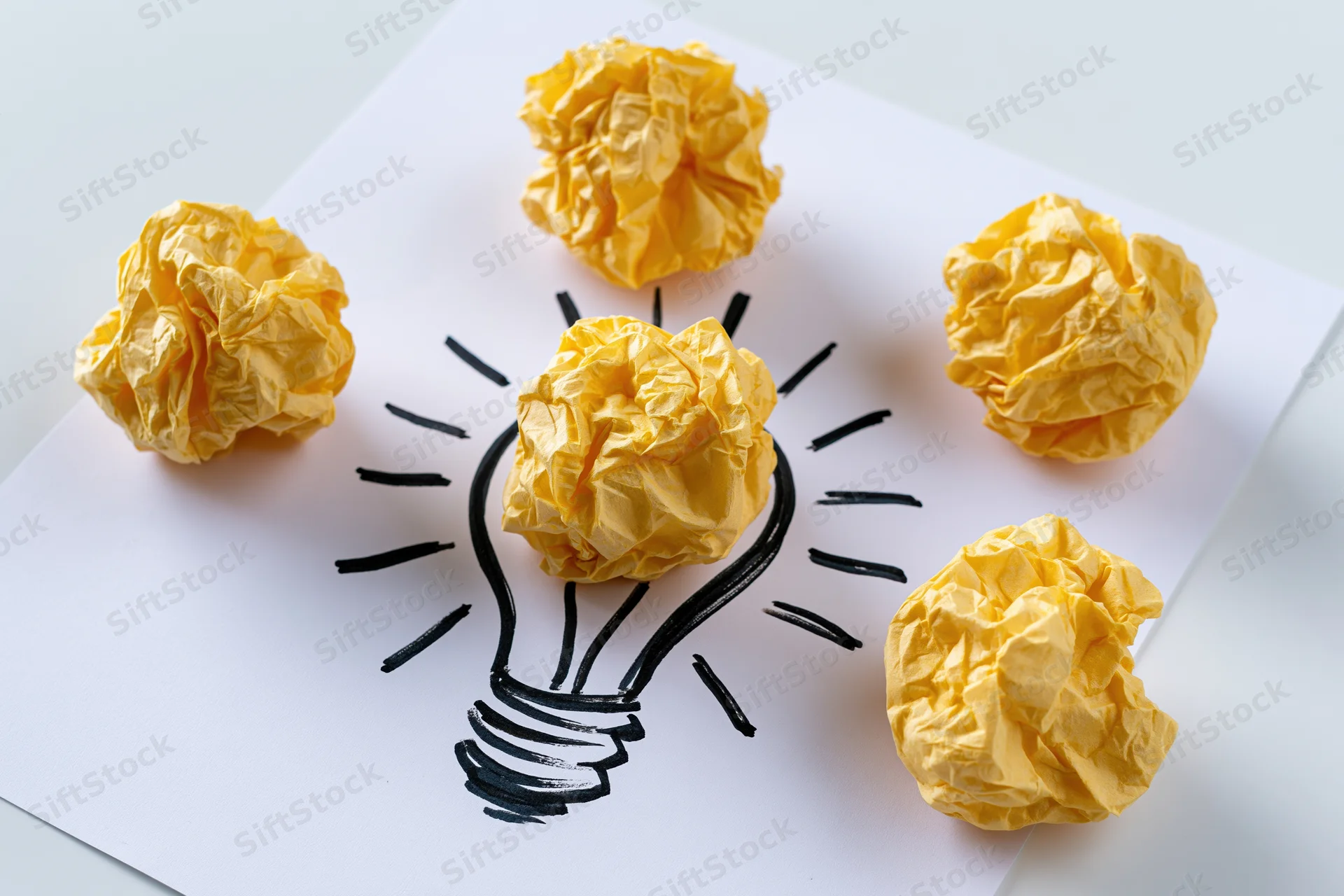 Crumpled yellow paper balls arranged around a hand-drawn lightbulb on white paper