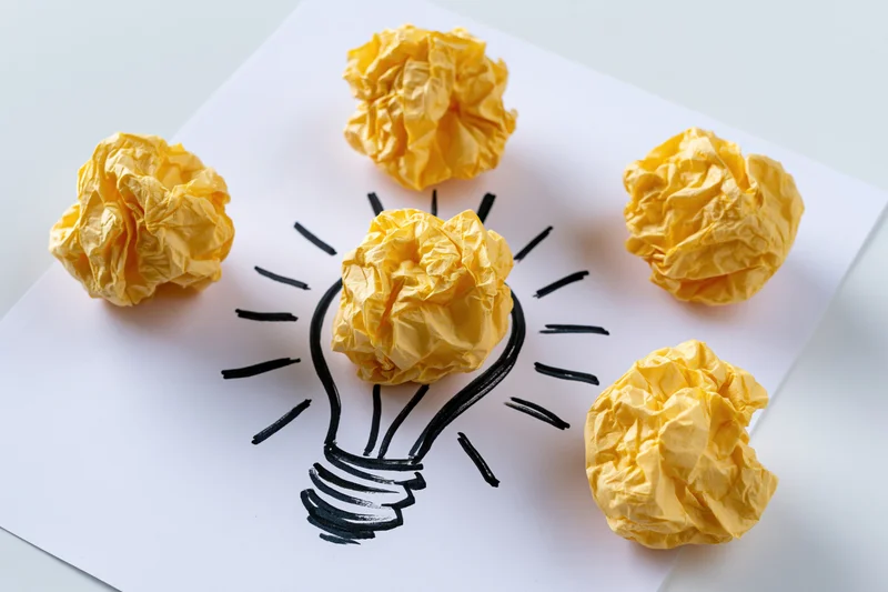 Crumpled yellow paper balls arranged around a hand-drawn lightbulb on white paper