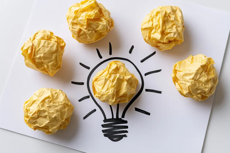 Crumpled yellow paper balls arranged around a hand-drawn lightbulb on white paper