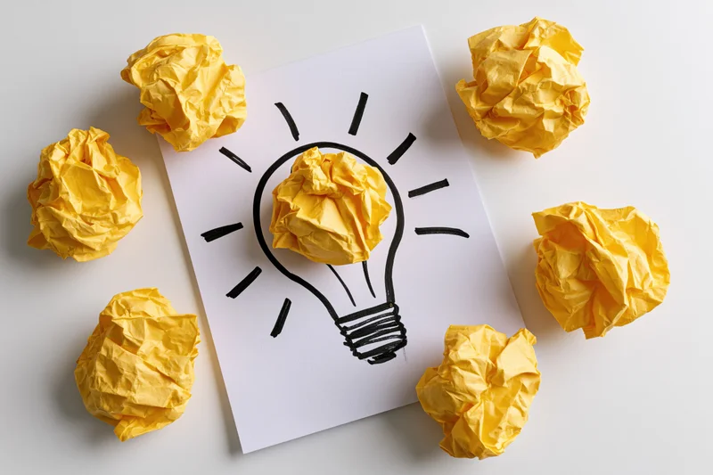 Crumpled yellow paper balls arranged around a hand-drawn lightbulb on white paper