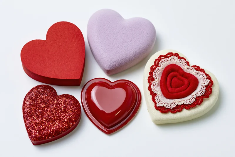 Five decorative hearts in various materials and colors arranged in a flat lay on white background