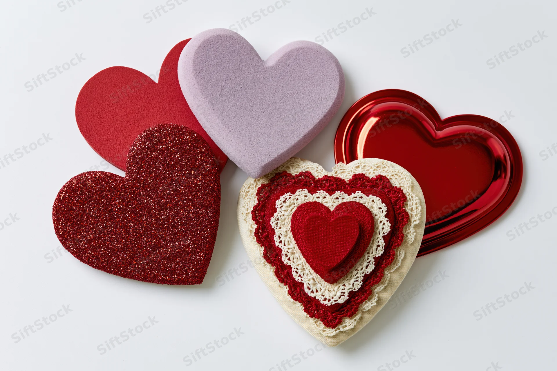 Five decorative hearts in various materials and colors arranged in a flat lay on a white surface