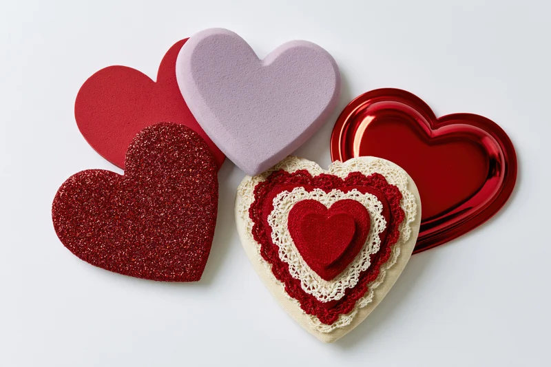 Five decorative hearts in various materials and colors arranged in a flat lay on a white surface