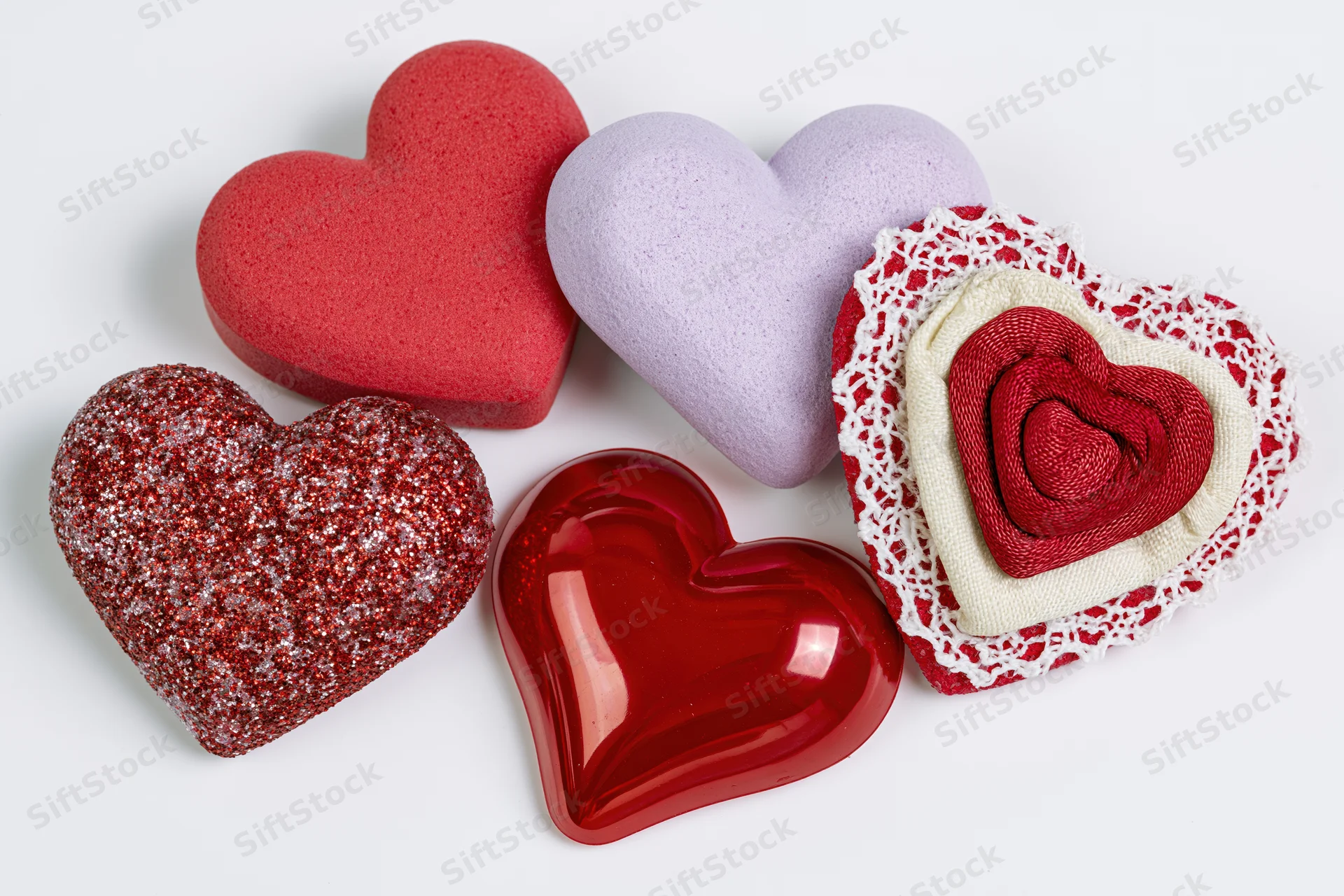 Five decorative hearts in various materials and colors arranged in a loose flat lay on white background