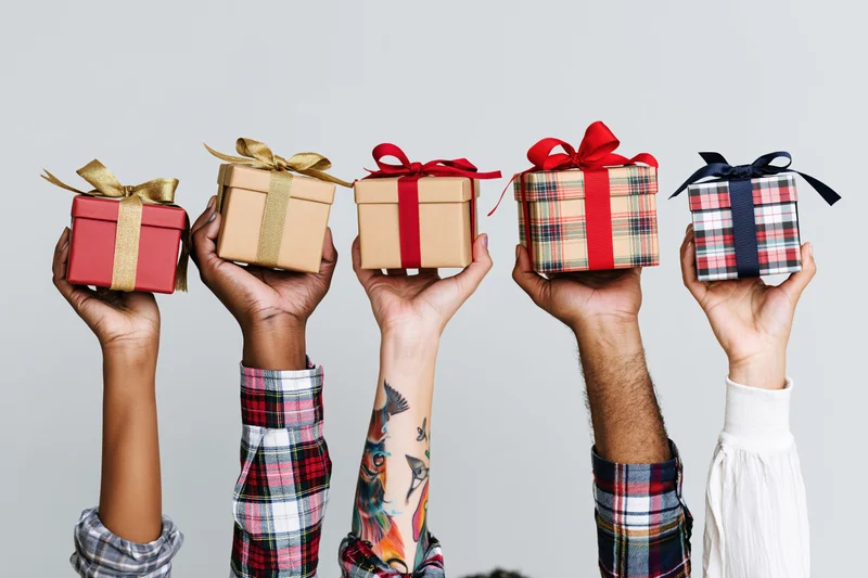 Five diverse hands holding wrapped gift boxes upward against a plain background