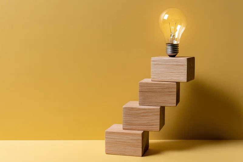 Wooden blocks arranged as ascending staircase with lightbulb on top against yellow background