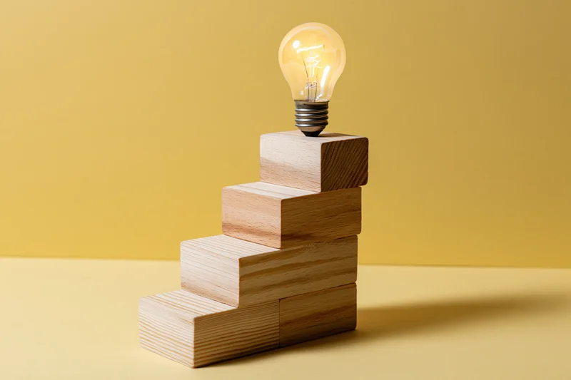 Wooden blocks arranged as ascending staircase with lightbulb on top against yellow background