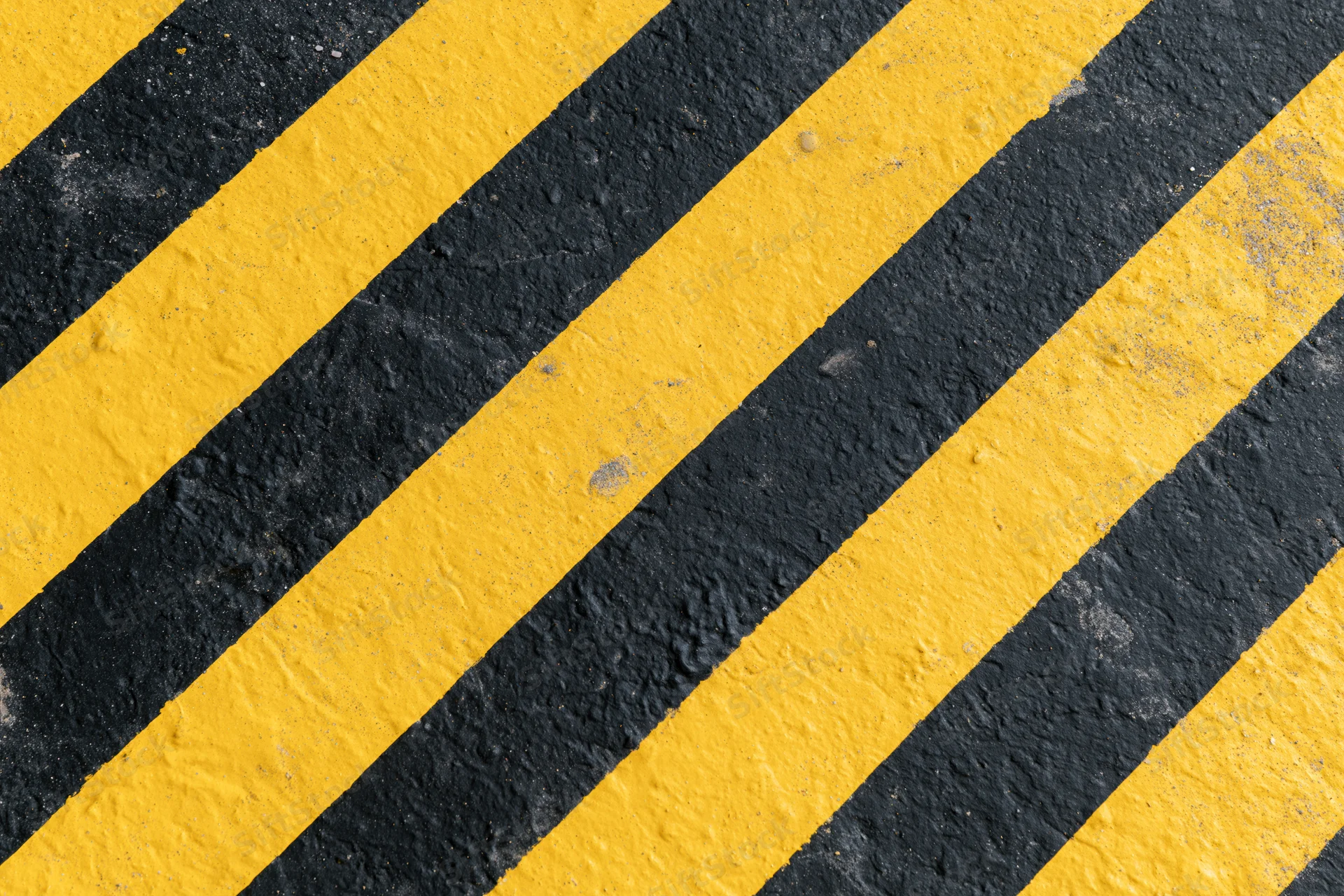 Diagonal yellow and black warning stripes painted on an industrial pavement surface
