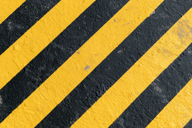 Diagonal yellow and black warning stripes painted on an industrial pavement surface