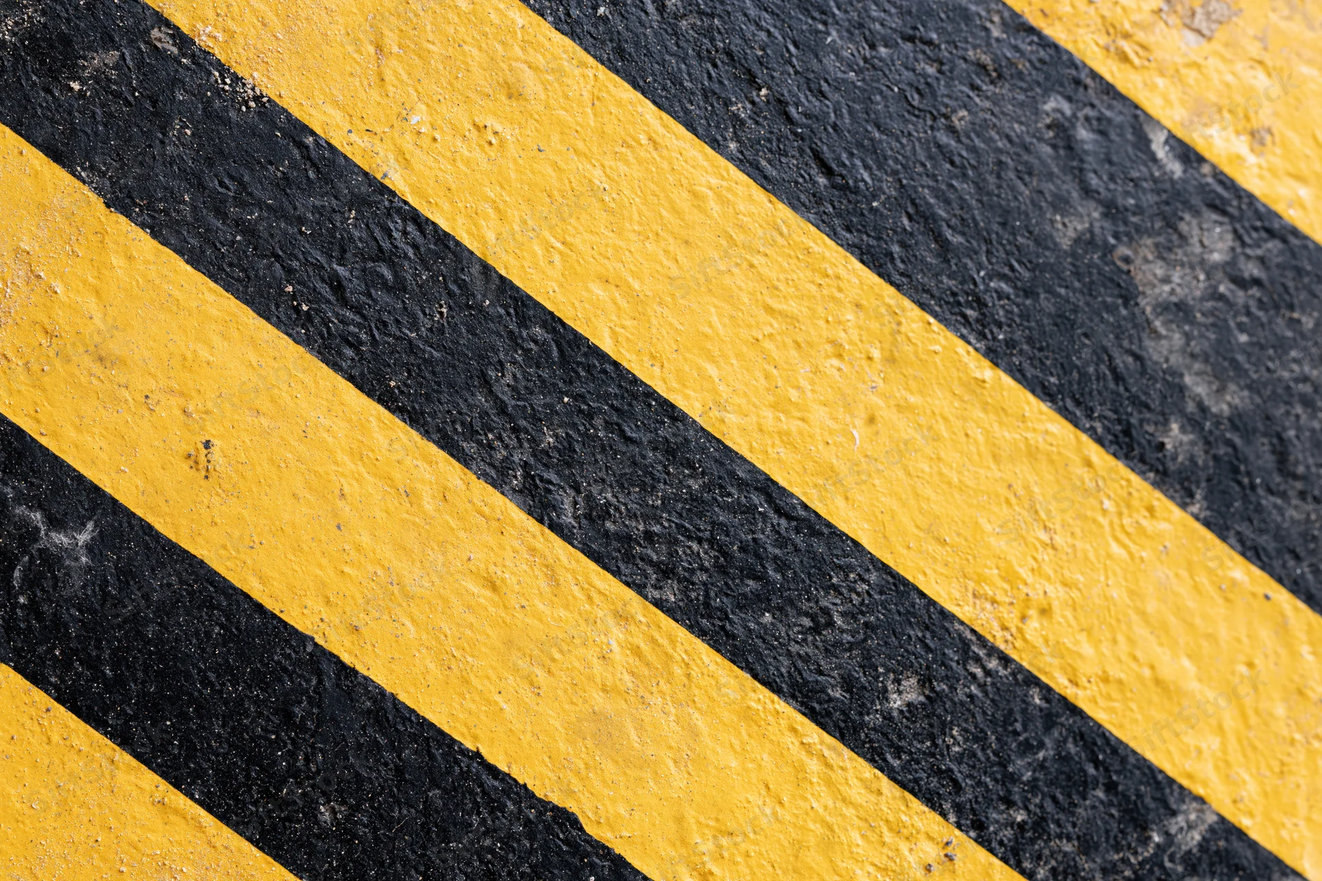 Diagonal yellow and black stripes painted on a rough asphalt surface