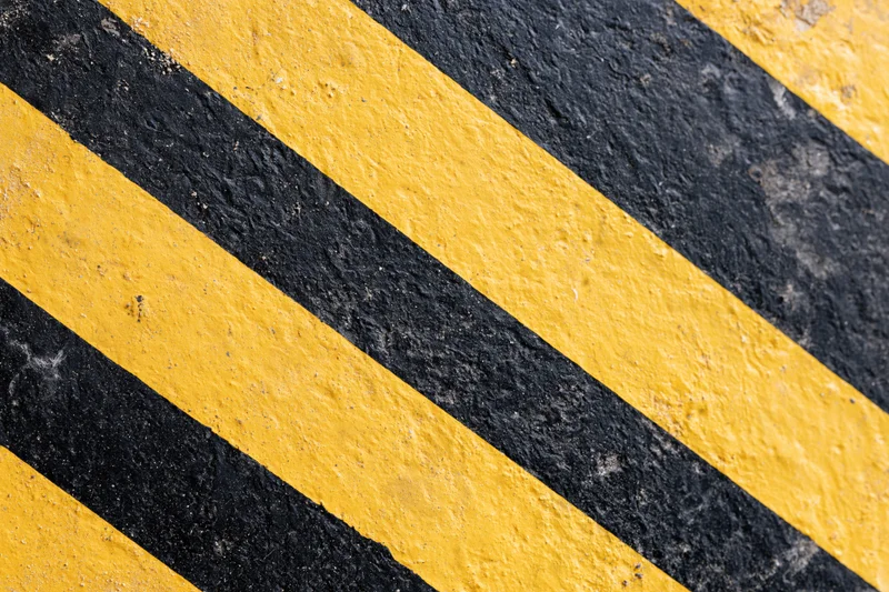 Diagonal yellow and black stripes painted on a rough asphalt surface
