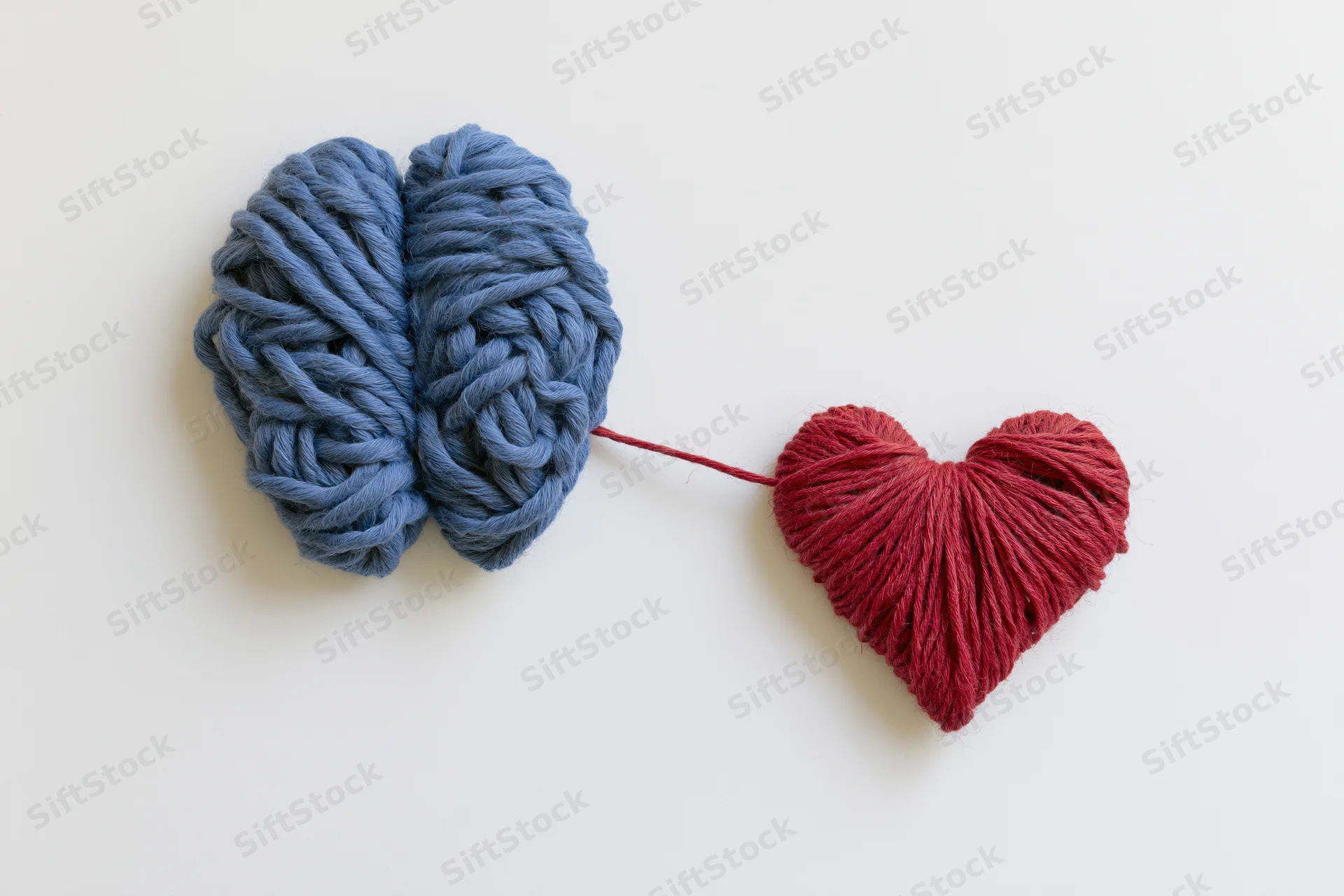 Blue yarn brain connected by red yarn to a red heart on white surface