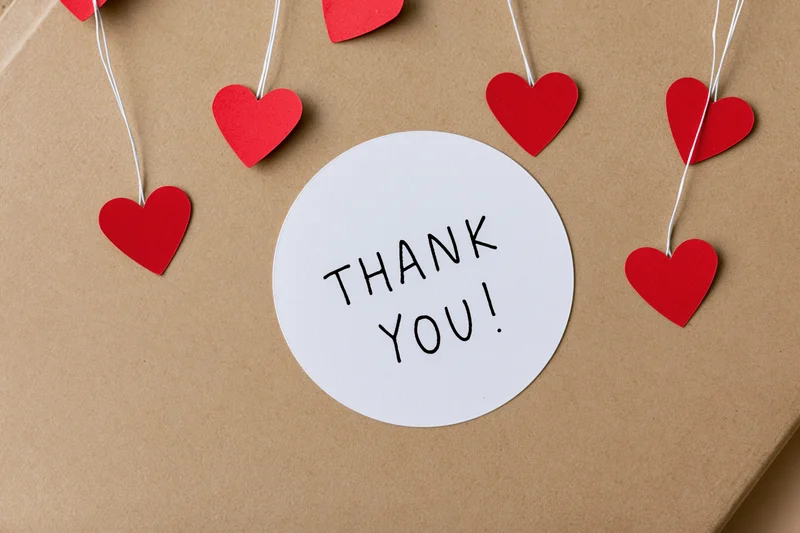 Round white sticker with thank you text on brown kraft paper surrounded by red hearts on strings