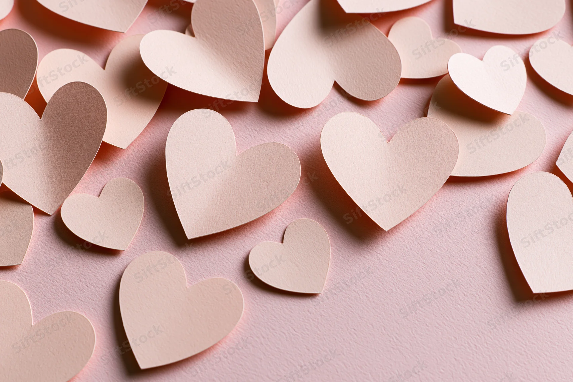 Paper heart cutouts scattered on a pink surface in a flat lay arrangement