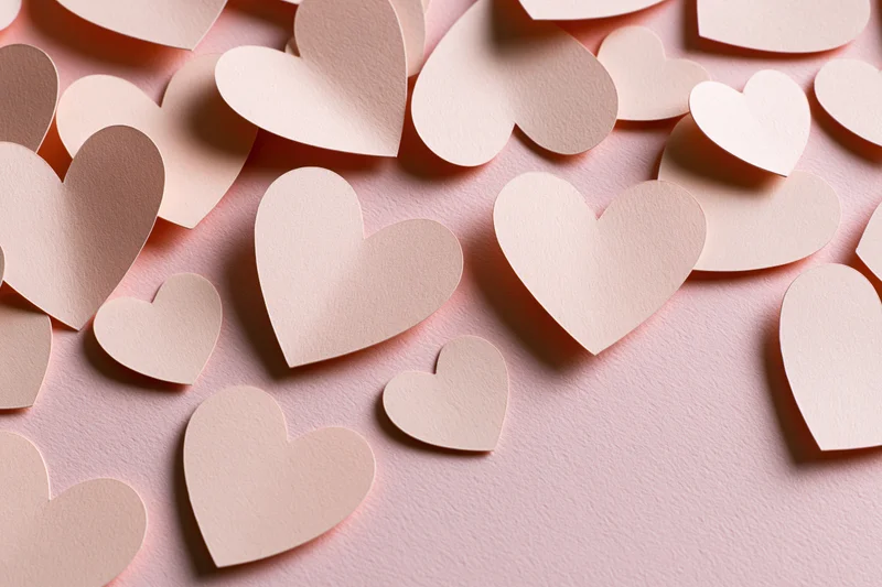 Paper heart cutouts scattered on a pink surface in a flat lay arrangement