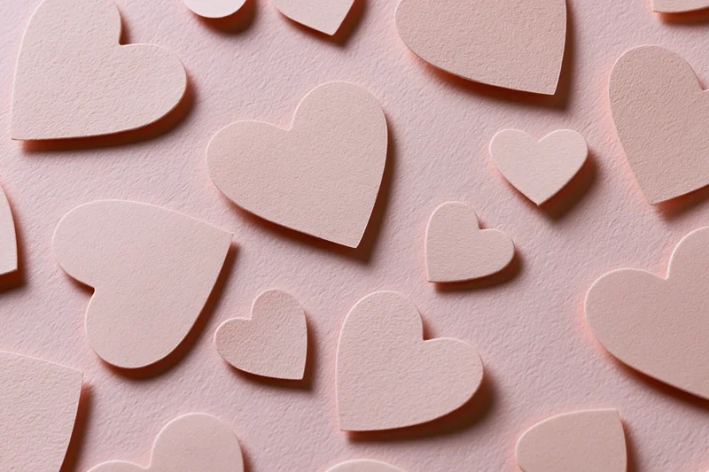 Paper heart cutouts scattered on a pink textured surface in a flat lay arrangement