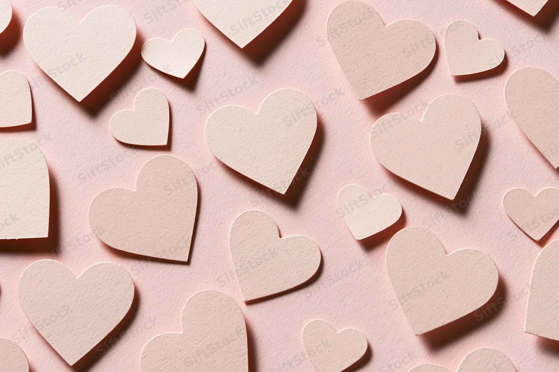 Paper heart cutouts scattered on pink surface in flat lay arrangement