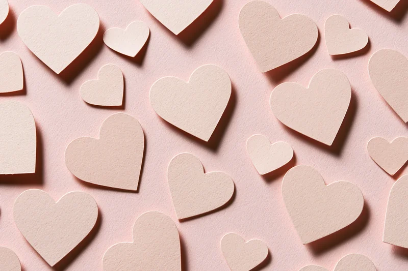 Paper heart cutouts scattered on pink surface in flat lay arrangement
