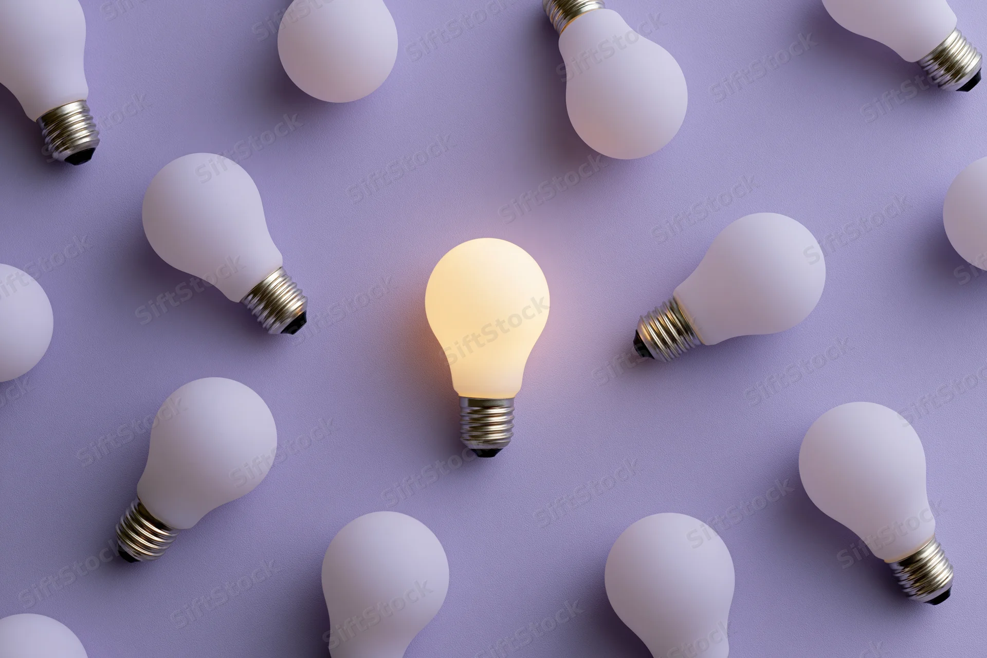 Single glowing lightbulb among unlit bulbs on purple surface