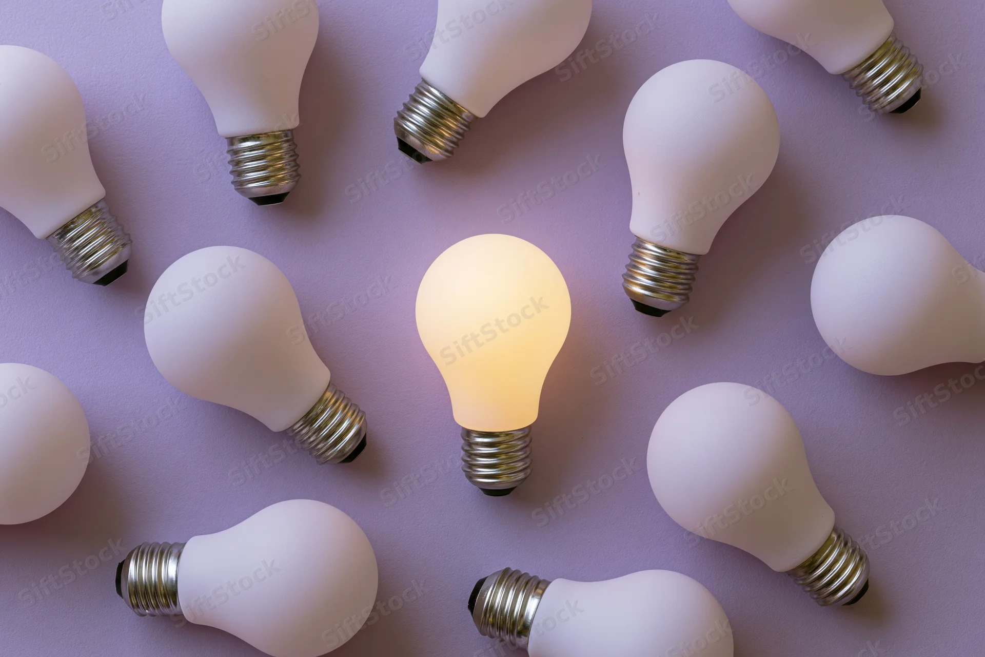 Multiple white light bulbs scattered on purple surface with one illuminated in center