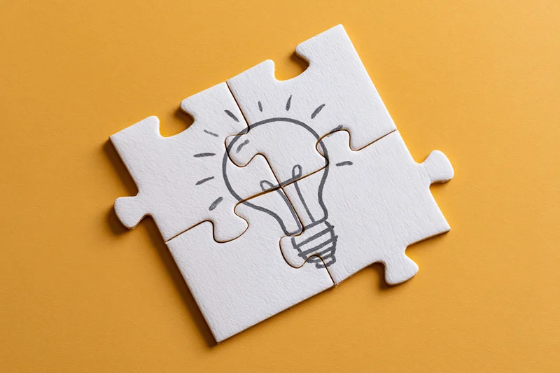 Four white puzzle pieces forming a hand-drawn lightbulb on orange background