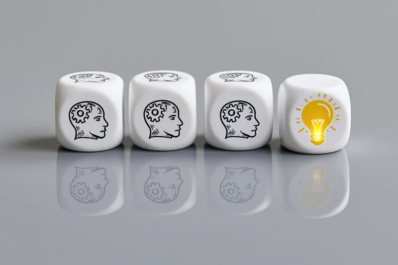 Four white dice in a row with brain and lightbulb symbols on a reflective gray surface