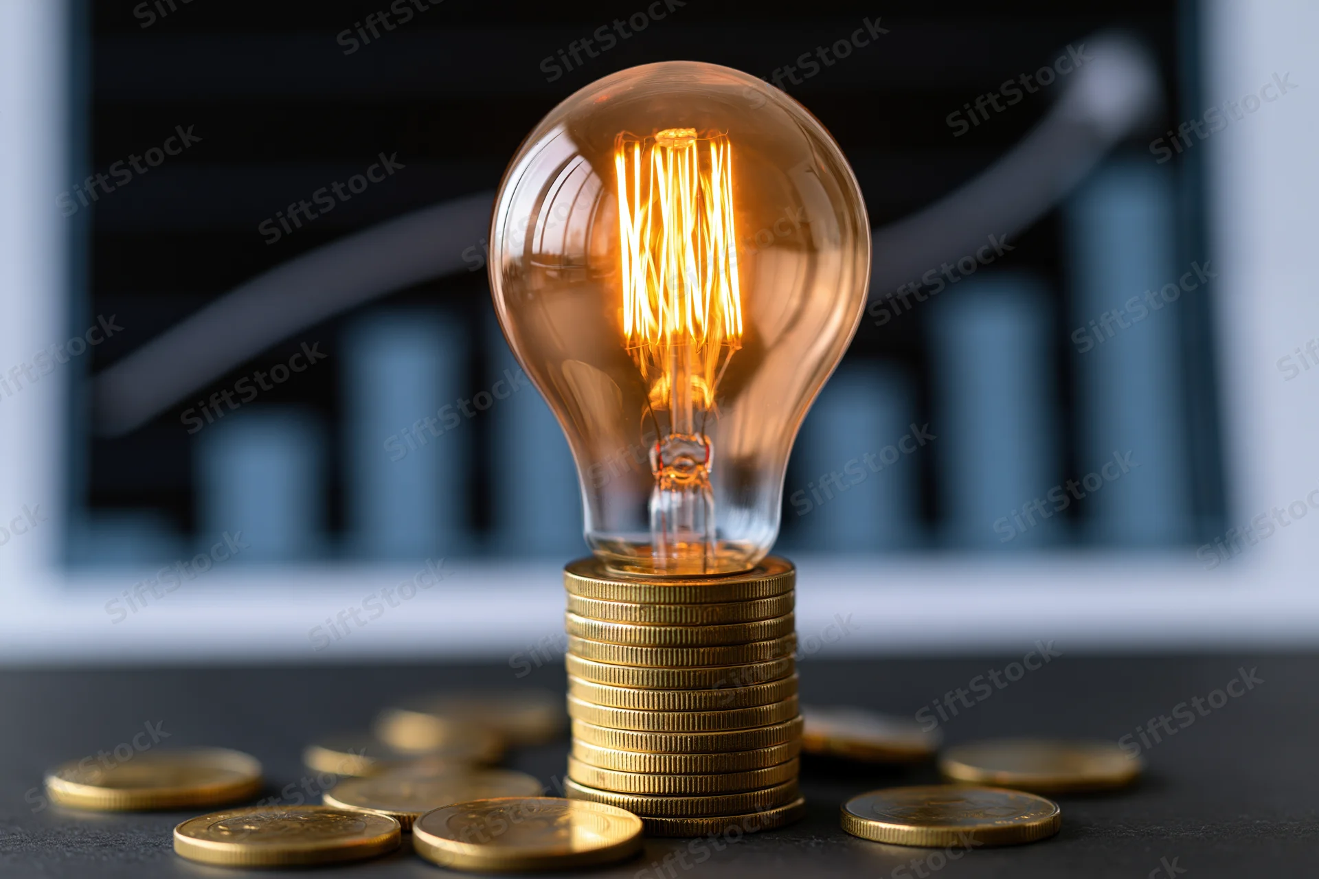 Glowing incandescent lightbulb on stack of gold coins with financial chart in background