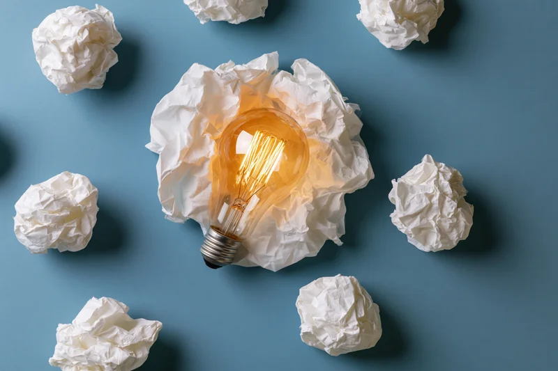 Glowing lightbulb nestled in crumpled white paper on blue background