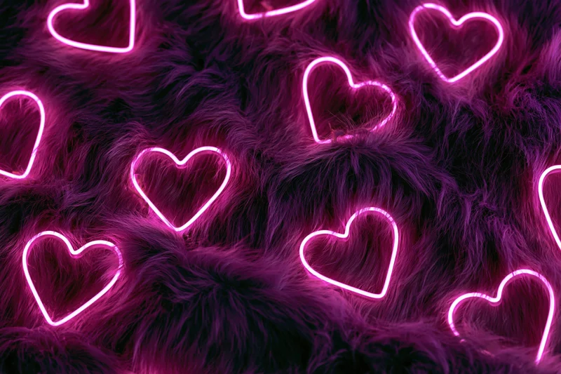 Glowing pink neon heart outlines scattered across a dark faux fur surface