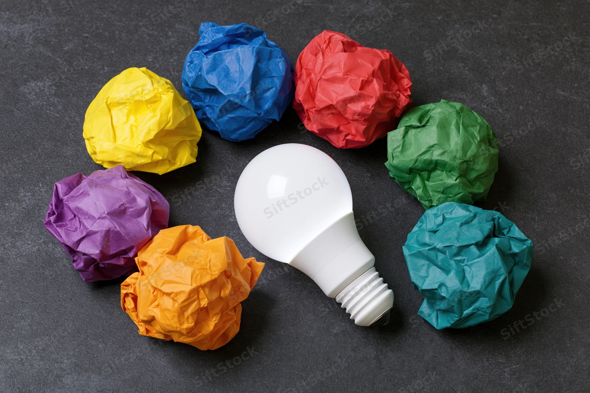 White led lightbulb surrounded by colorful crumpled paper balls on dark surface