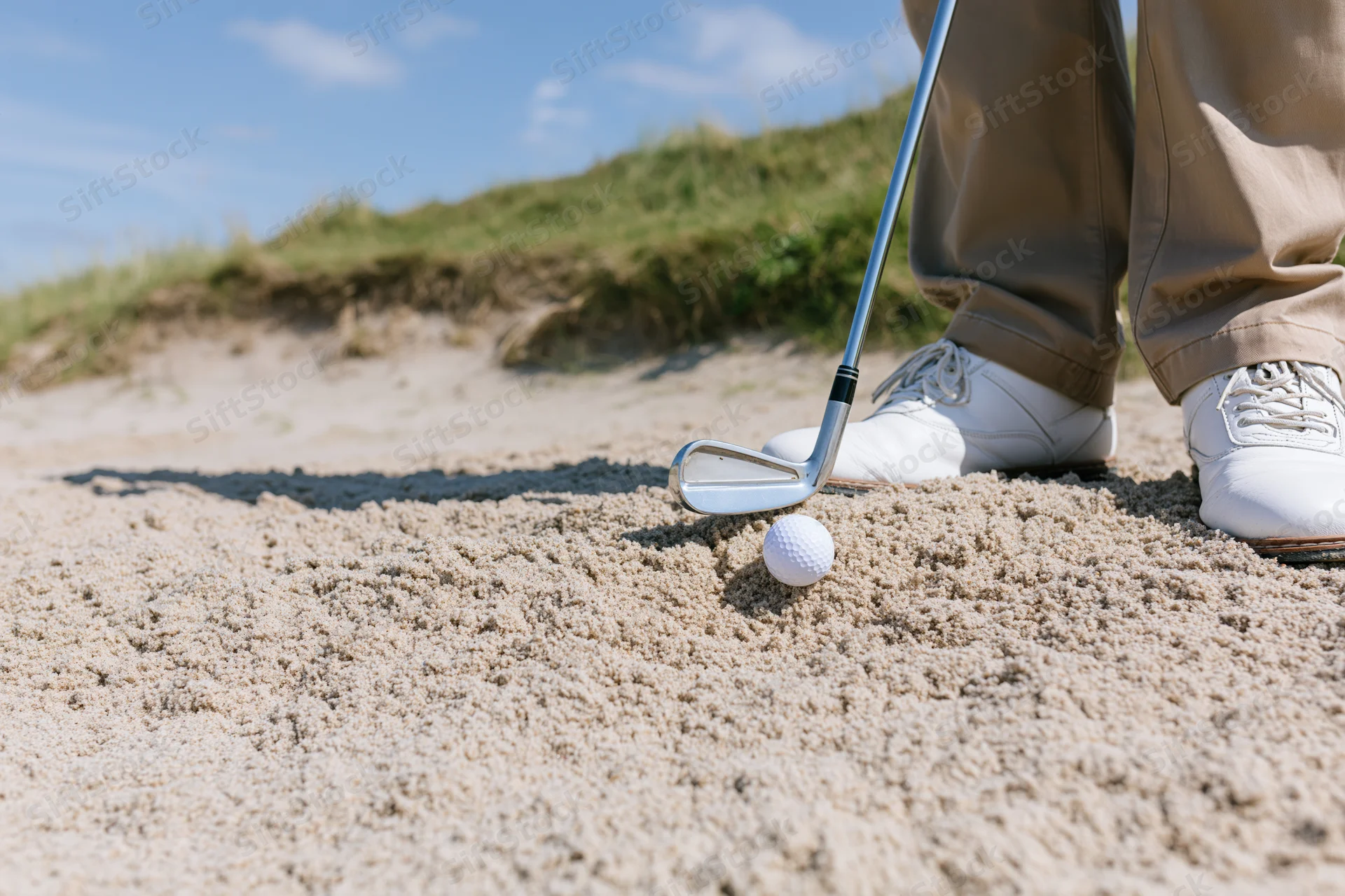 Golfer standing in sand bunker with iron club head near white golf ball on course