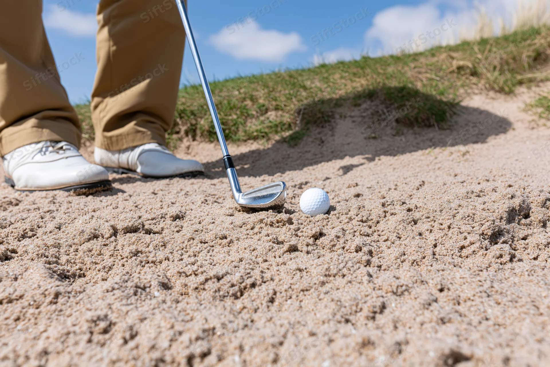 Golfer standing in sand bunker with iron club near golf ball on course