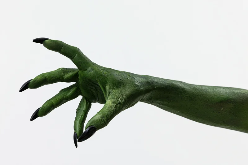Green-painted hand with black claws reaching forward against white background