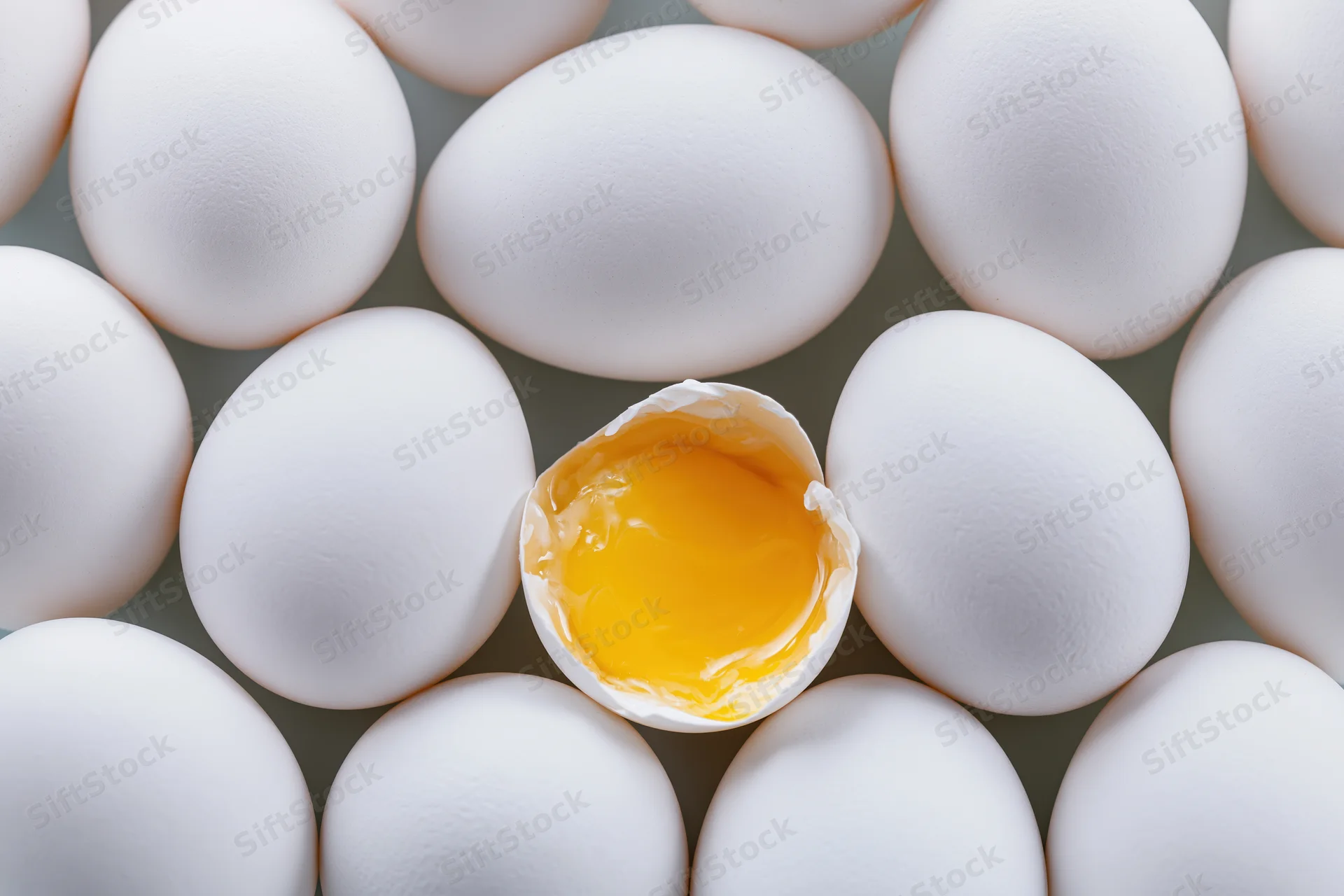 Grid of white eggs with one cracked open revealing yolk at center
