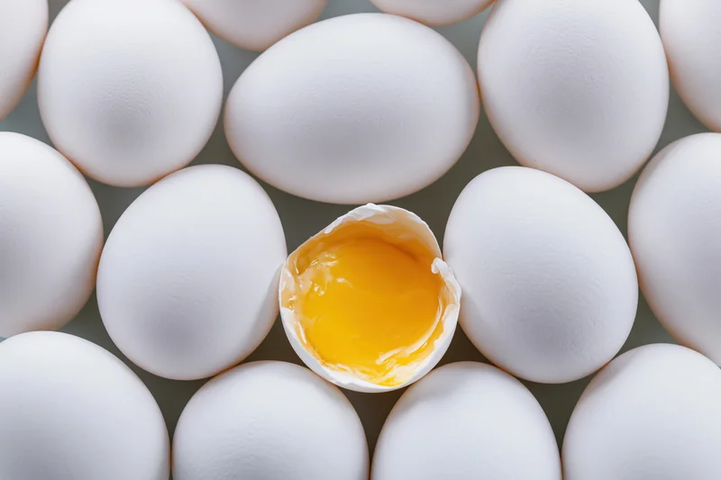 Grid of white eggs with one cracked open revealing yolk at center