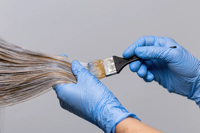 Hairdresser applying dye to hair with brush while wearing blue gloves