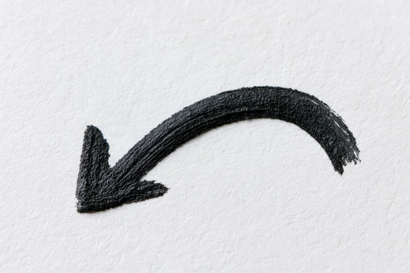 Hand-drawn black ink arrow curving downward left on white paper