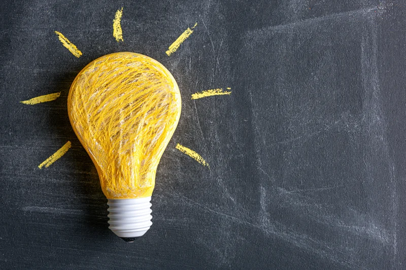 Chalk-drawn lightbulb with radiating lines on a blackboard surface