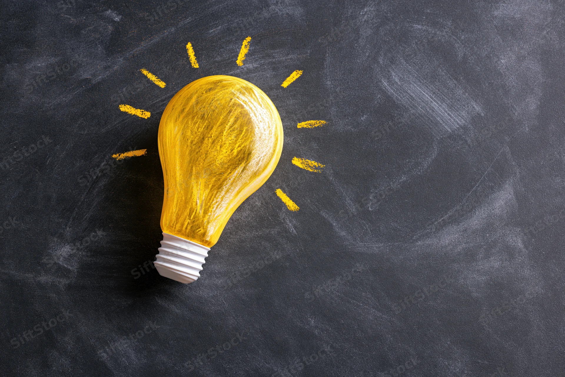 Yellow chalk lightbulb drawn on dark blackboard surface with radiating lines