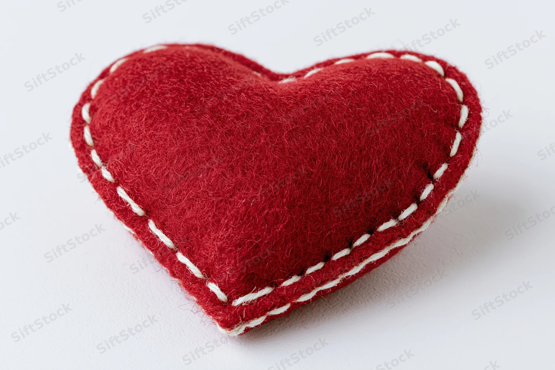 Handmade red felt heart pillow centered on plain white background