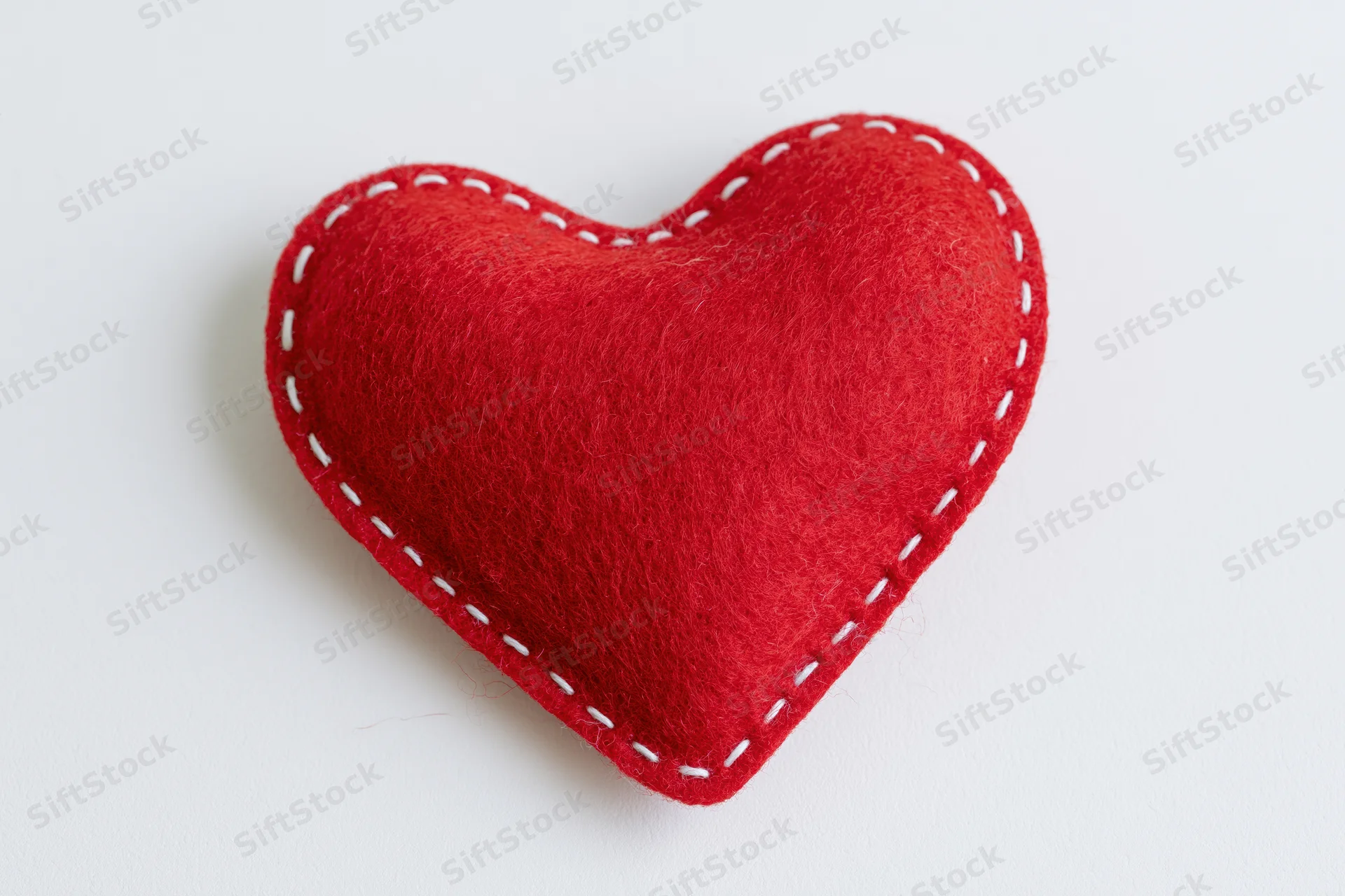 Red handmade felt heart pillow centered on white background