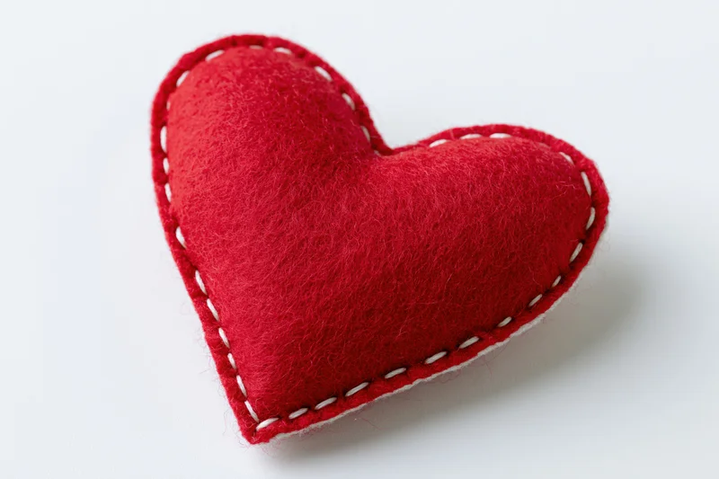 Handmade red felt heart pillow centered on plain white background