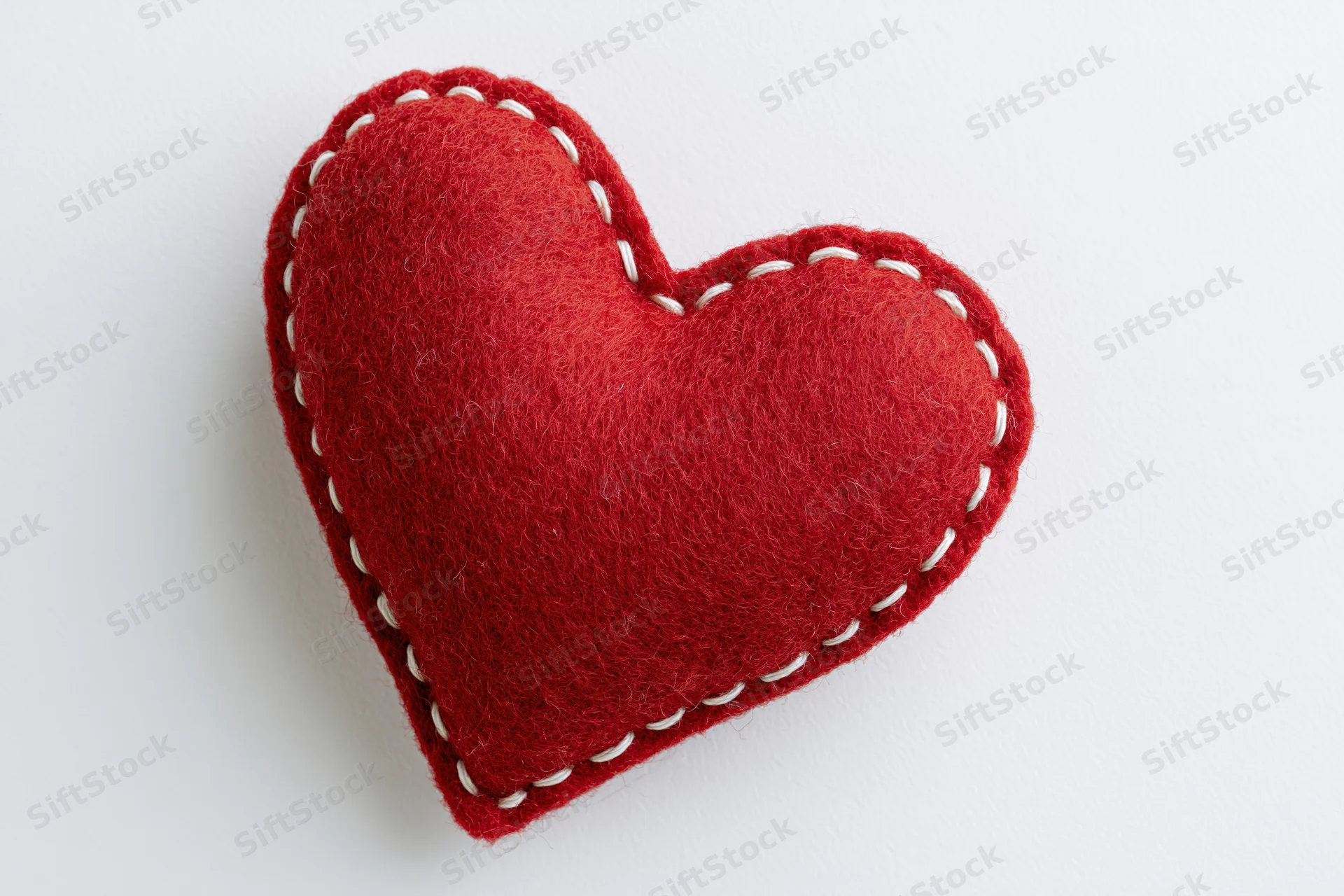 Handmade red felt heart pillow centered on plain white background