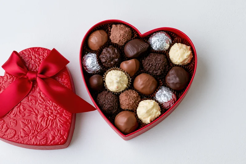 Heart-shaped chocolate gift box open on white surface with red ribbon on lid