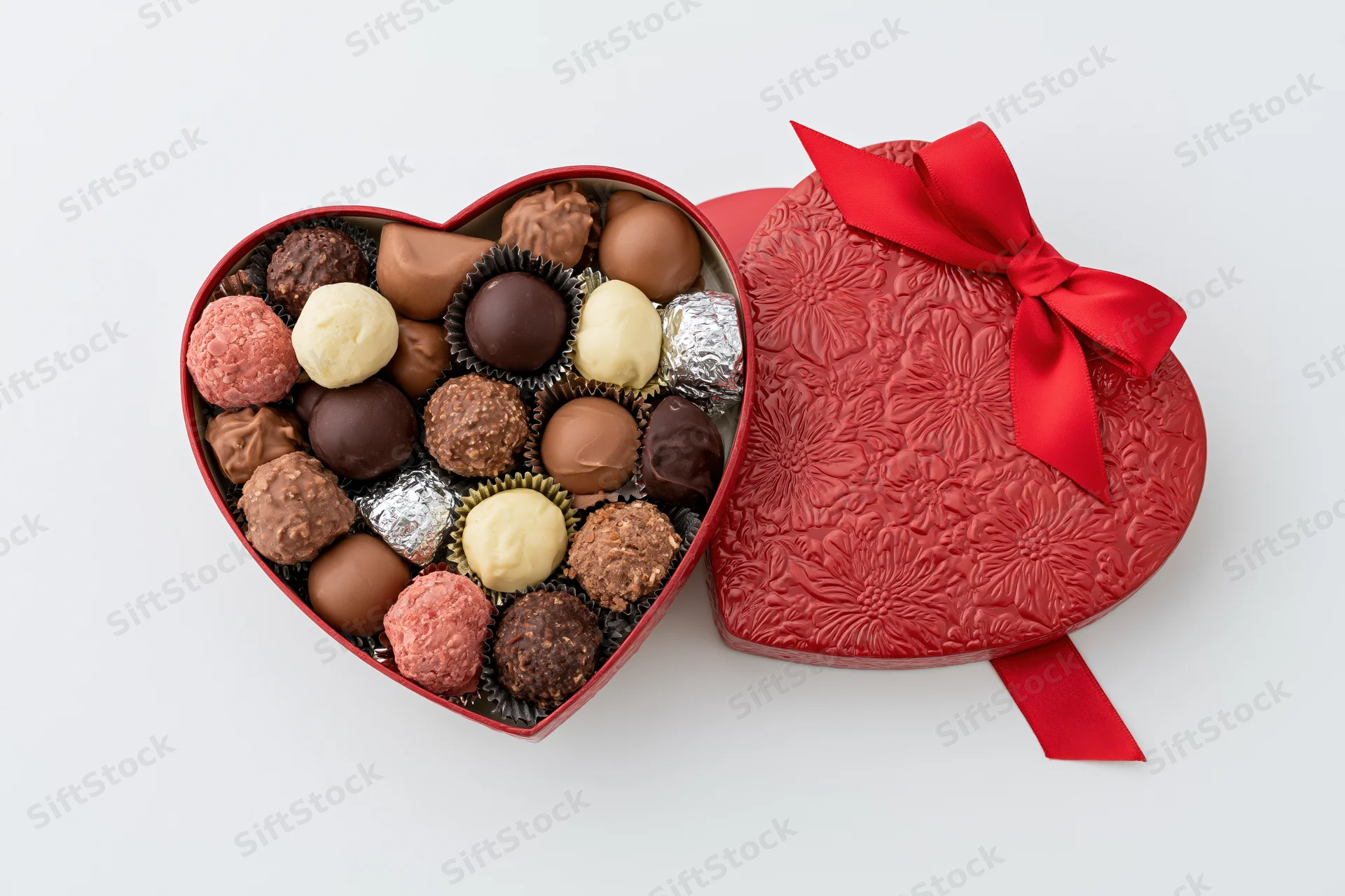 Heart-shaped chocolate gift box open with assorted candies inside on white background