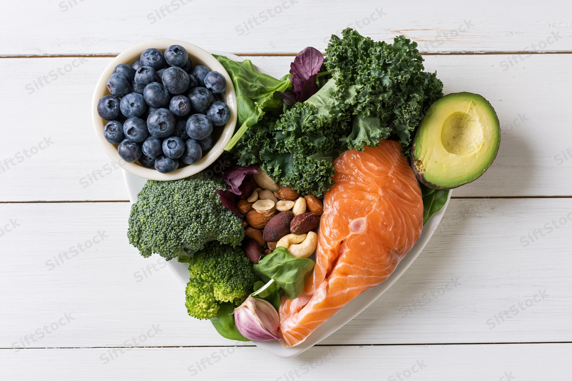 Heart-shaped arrangement of healthy whole foods on a white wooden table