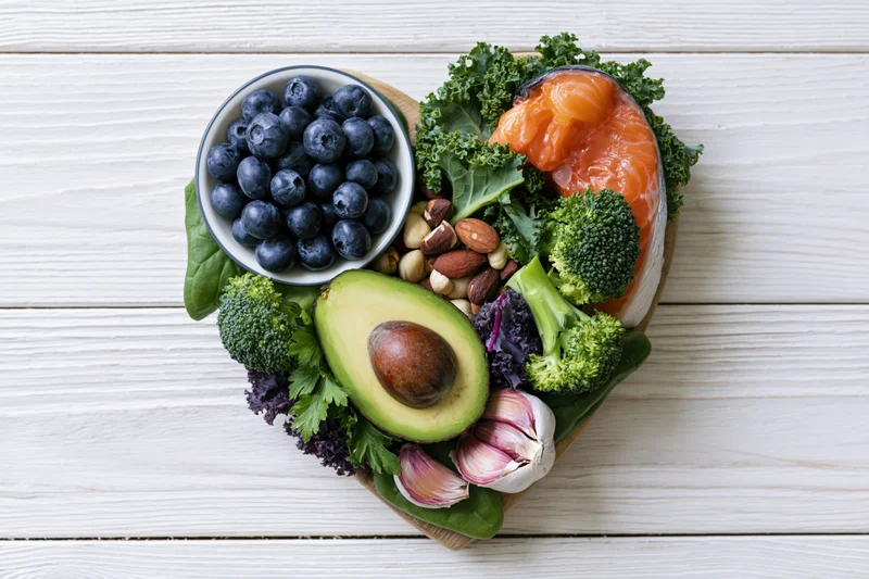 Heart-shaped arrangement of healthy whole foods on a white wooden surface