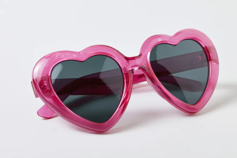 Heart-shaped pink plastic sunglasses on white background